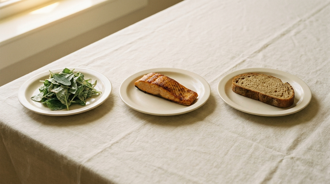 Three small cream ceramic plates in a horizontal row on cream linen, holding leafy salad, grilled protein, and a slice of artisan bread — the food-sequencing editorial hero showing fiber, protein, then carbohydrate eating order